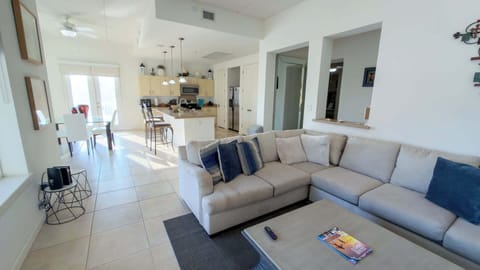 Open-Plan Living & Dining Area
Spacious living room flows seamlessly to dining and kitchen with plush sectional sofa, ceiling fans, and abundant natural light. Gather for games or meals near balcony doors—cozy coastal vibes for unforgettable stays!