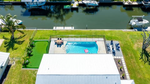 Aerial view of the pool, putting green, fire pit, and private canal access — your own waterfront oasis.