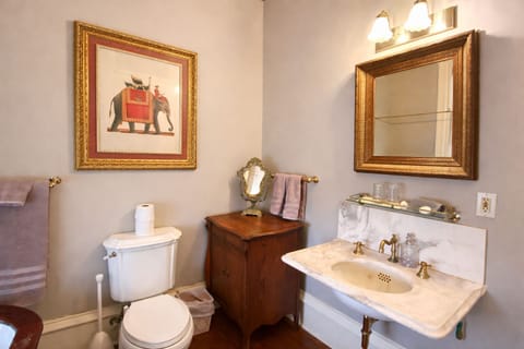 Bathroom view showing marble sink, toilet, framed artwork, and vintage mirror.
