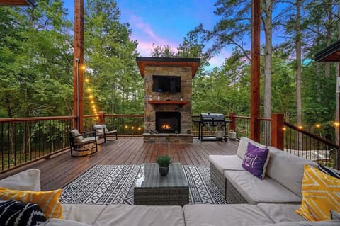 Spacious outdoor deck with a cozy fireplace, TV and surrounded by forest view.