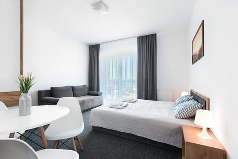 A bright bedroom with two neatly made beds, soft gray accents, and large windows letting in natural light.
