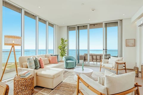 Step into your bright, open living room where floor-to-ceiling windows frame endless ocean views. Sink into the plush seating, feel the sea breeze from your private balcony, and let the calming blue horizon become your daily backdrop.