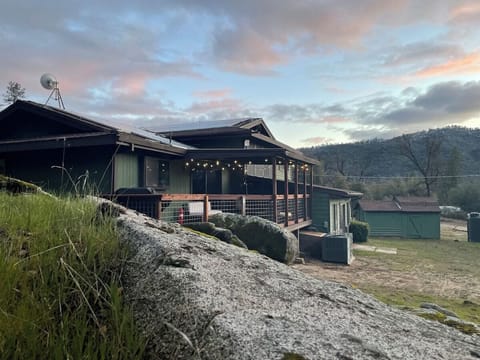 Back view of home. Large deck with grill and cushioned chairs and ottomans.
