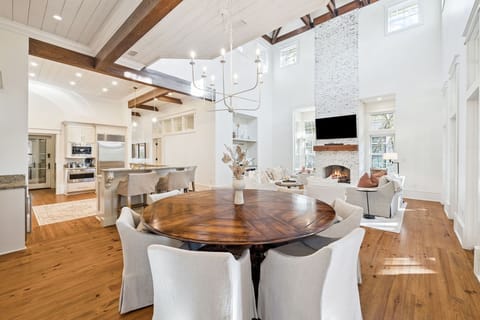 Step into your elegant open-concept haven where soaring ceilings and rich wood beams frame intimate dining moments by the cozy fireplace.