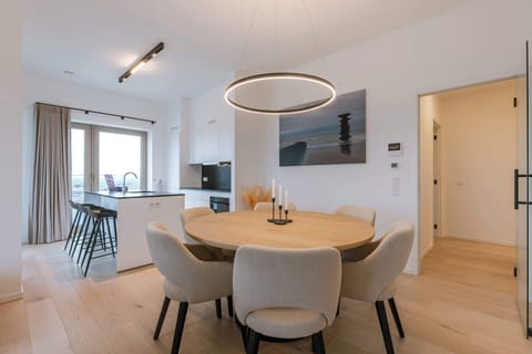 The heart of the home: a bright, open-plan dining area with a stylish round wooden table, perfectly positioned under a designer halo light.