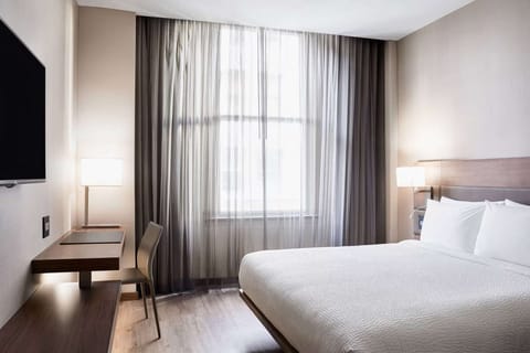 Bright room with soft bed, window curtains, and TV on the wall