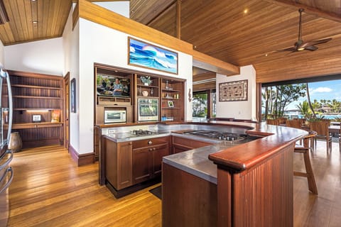 Your chef's paradise features rich wood cabinetry, premium appliances, and stainless steel countertops with tropical views just beyond.