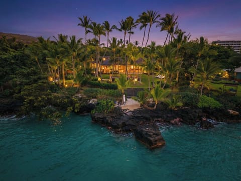 Hahalua Bay Villa sits oceanfront amid tropical palms with turquoise waters and volcanic rock formations creating a stunning Hawaiian setting.