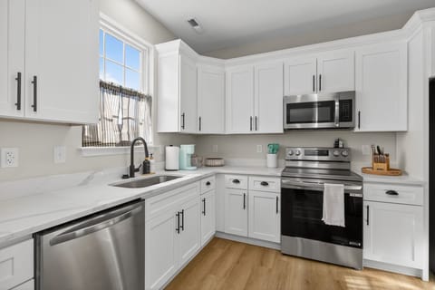 This kitchen angle shows off the bright window and polished stainless appliances. White cabinets make the entire space shine. 