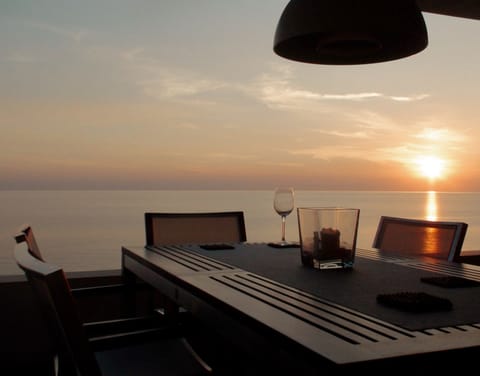 Outdoor dining table facing the sea at sunset, with open horizon views