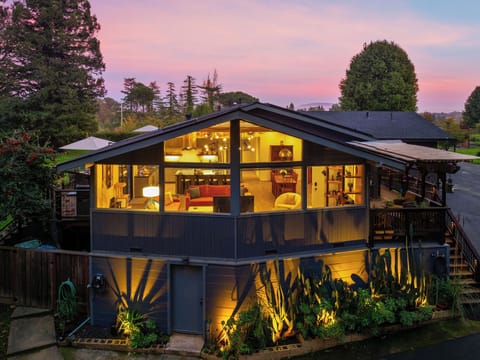 Modern vacation rental with floor-to-ceiling windows showcasing warm interiors beneath a stunning sunset sky in a peaceful residential setting.