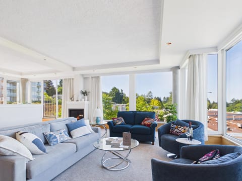 Corner living room with floor-to-ceiling windows, white curtains, gas fireplace, and a mix of blue and gray upholstered seating.