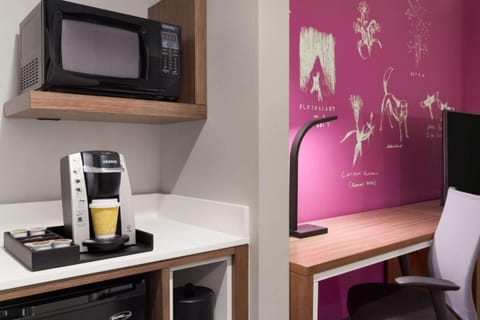 Coffee station with microwave beside desk and magenta wall.