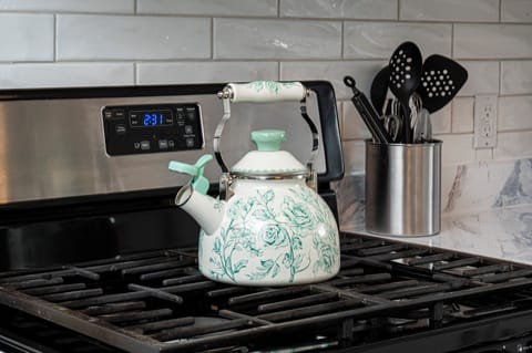 Stainless gas range with tea kettle, subway tile, utensils, and kitchen counters