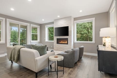 Cozy up in your elegant living room with modern fireplace, plush seating, and forest views through large windows.