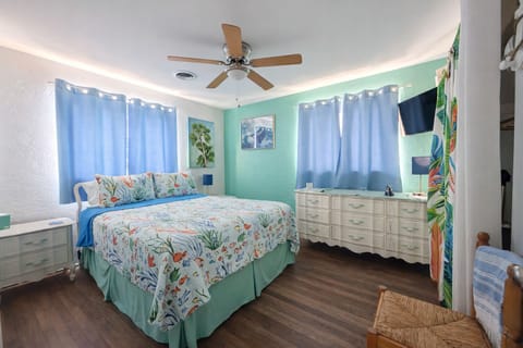Bright coastal bedroom with comfy queen bed, TV, dresser, and ceiling fan.