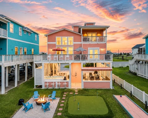 Beachfront home exterior with balcony, covered patio, putting green, fire pit area, and ocean-view backyard.