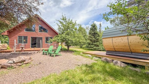 A charming red log cabin set amid mature trees and greenery with an outdoor sauna nearby for ultimate relaxation after exploring the natural surroundings.
