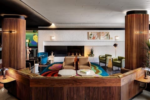 A cozy lounge area in The Drake Hotel highlights its art-forward design with a stunning fireplace, surrounded by bold colors and unique seating.