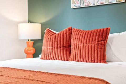 Inviting bedroom with a warm, modern design — featuring terracotta pillows, cozy bedding, and soft lighting that creates a relaxing ambiance.