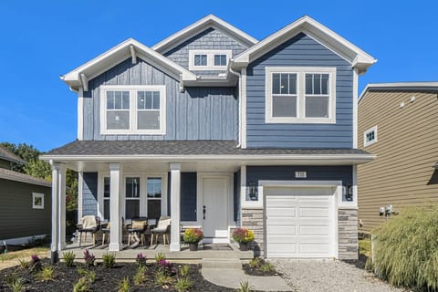 Beautiful two-story coastal-style home with a welcoming front porch, outdoor seating, and bright blue siding the reflects the charm of South Haven.