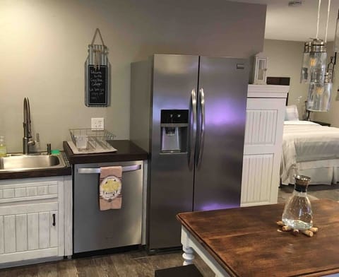 This beautiful kitchenette ensures maximum convenience, featuring a full-sized stainless steel French-door refrigerator and dishwasher. The space flows beautifully into the bedroom area, framed by a stylish decorative mantel and rustic lighting.