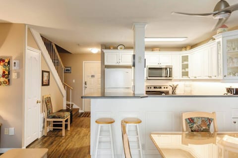 Kitchen area with a counter, stools, and sleek white cabinets.

