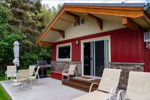 Cozy red house with a porch, deck, and outdoor furniture, nestled among trees.