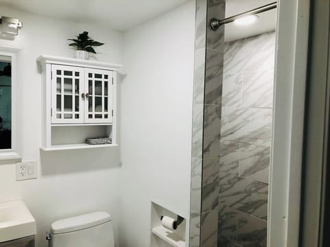 Step into this luxurious and bright shower, featuring gorgeous, modern marble-style tiling and clean glass enclosures. The adjacent vanity area includes a charming cabinet for organized storage, completing this beautiful guest space.