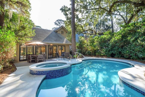 A luxurious private pool and integrated spillover hot tub surrounded by a spacious concrete deck. The area is framed by mature trees and professional landscaping, offering a secluded oasis for relaxation.

