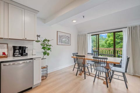The dining area sits between the kitchen and balcony doors, with treetop views just outside.