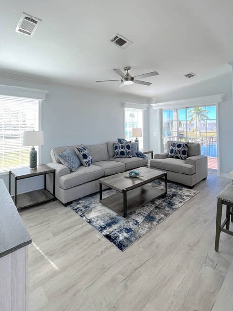 Relax in your spacious living room with plush gray seating, modern décor, and natural light streaming through large windows.