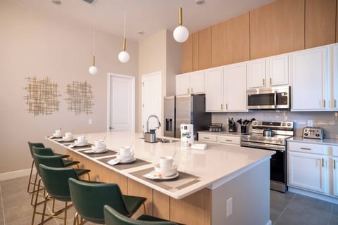Experience the heart of the home in this stylish kitchen, featuring sleek white and wood cabinetry, a spacious island with elegant green bar stools, and modern pendant lighting that enhances the warm ambiance.