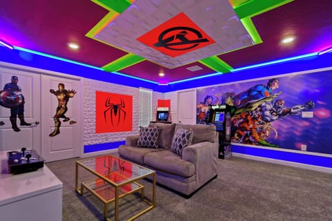 Enter a lively game room filled with vibrant superhero murals and playful neon lights. A cozy gray sofa offers a spot to relax, while a sleek glass coffee table adds a stylish touch to this colorful escape.
