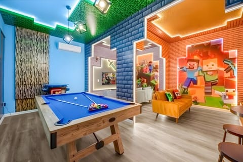 Enter our lively game room, featuring bright blue walls and a playful green ceiling with a custom mural that inspires creativity. Enjoy a game at the sleek pool table or unwind on the cozy orange couch for an entertaining evening.