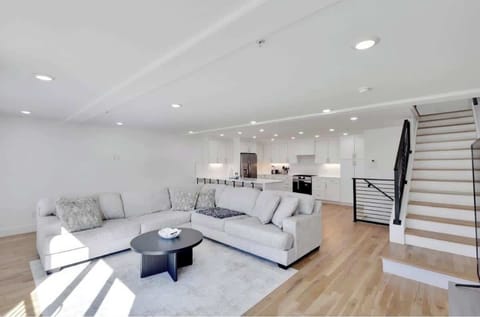 Bright, open living area with a cozy sectional, modern decor, and plenty of natural light, flowing into a sleek kitchen with hardwood floors and contemporary style.
