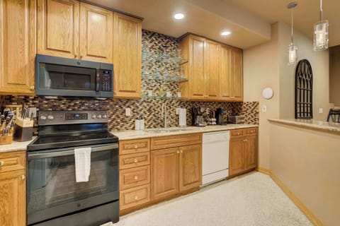The fully equipped kitchen features professional-grade appliances, including a smooth-top range and built-in microwave. Sleek cabinetry and a decorative tile backsplash create a modern and functional space for preparing vacation meals.