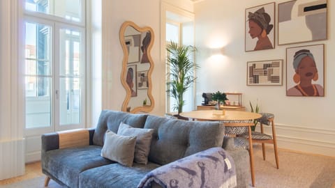 Stylish and sun-drenched, the living room pairs soft textiles with curated art and a playful designer mirror, inviting you to relax in refined comfort. #PortoApartment #DesignStay #NaturalLight