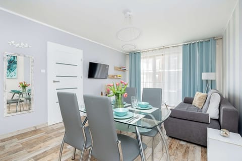 A contemporary dining area with a round table and stylish chairs. Large windows illuminate the soft-colored interio