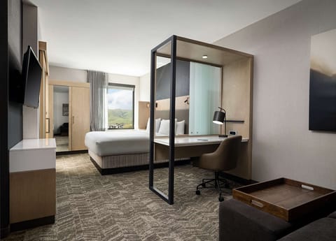 Room with king bed, desk, and view of green hills through window