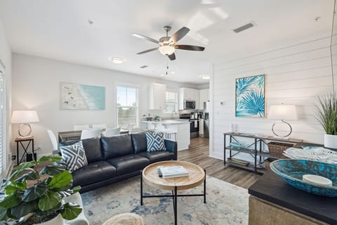 Relax in your bright, coastal-inspired living space featuring a comfy leather sofa, tropical artwork, and modern amenities.