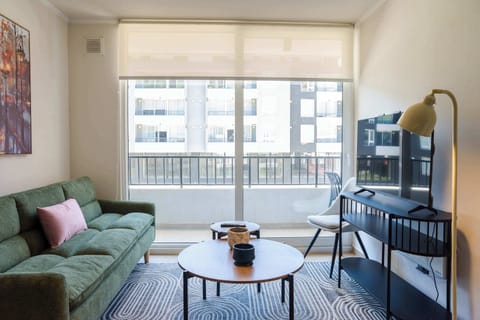 Bright and cozy living room with a comfy sofa and large windows offering city views, perfect for relaxation.