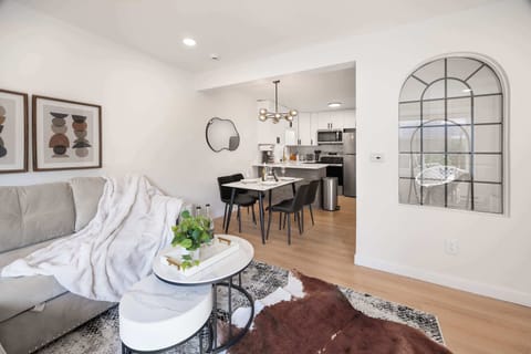 Chic and cozy living space with soft furnishings, stylish decor, and an open layout leading into a modern kitchen and dining area, perfect for relaxing or enjoying a meal.