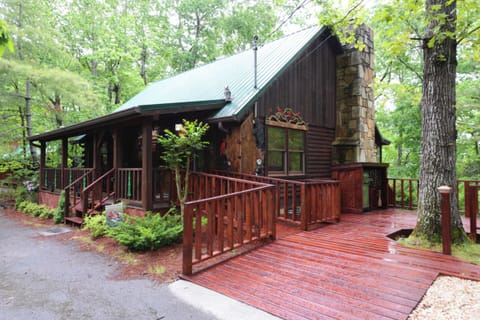 Charming log cabin nestled among towering trees, featuring a welcoming wraparound deck and stone chimney for cozy mountain retreats.