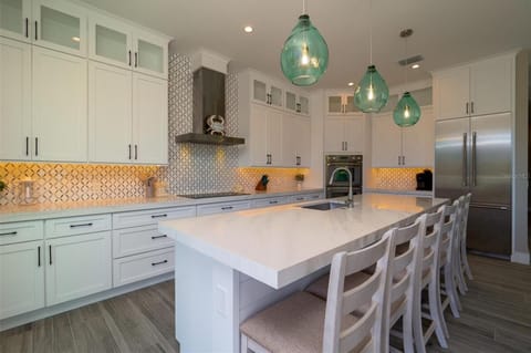 Your gourmet kitchen features stunning white cabinetry, marble countertops, and elegant turquoise pendant lights that cast a warm glow over the spacious island.