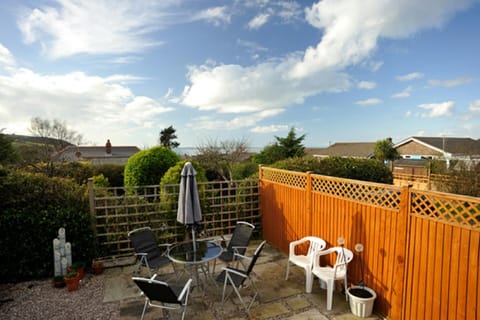 Patio with metal table and chairs, closed umbrella, and orange wooden fence under cloudy sky