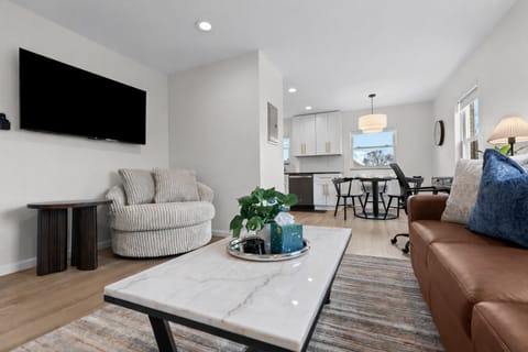 Spacious, light-filled living area with modern seating, large smart TV, and open flow to the kitchen and dining space—ideal for relaxing or entertaining.
