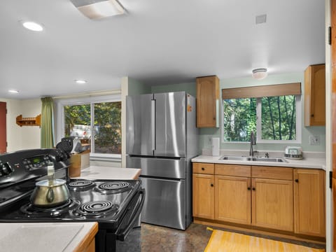 Cook your favorite meals in this bright, fully equipped kitchen with modern appliances, warm wood cabinets, and peaceful garden views.
