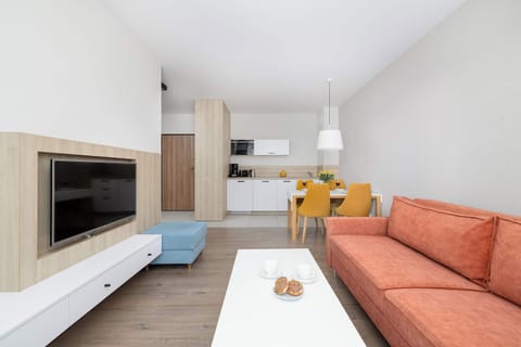 An open-plan living room and kitchen with a sofa in warm tones, a white media console, and a dining table in the background.