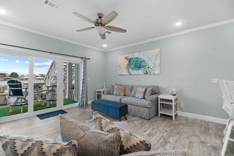 Coastal living area at Pescador Landing, Perdido Key – featuring a sea turtle accent wall, comfortable seating, and sliding glass doors to the waterfront deck. Steps from FloridaBama.